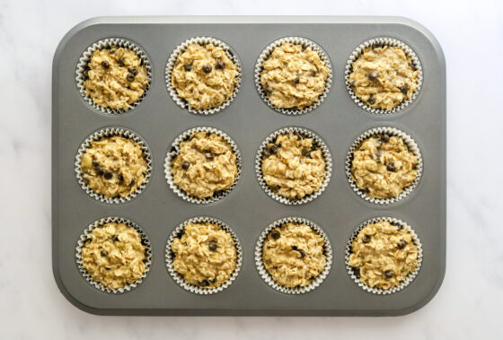 Peanut butter banana oatmeal mixture divided into 12 cupcake tin lined with paper liners.