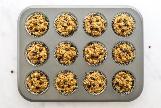 Twelve baked peanut butter banana oatmeal cups in a muffin tin.
