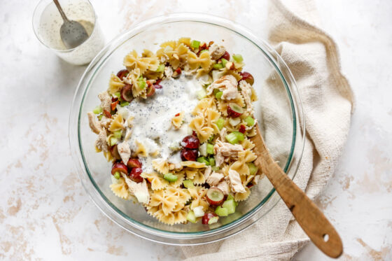 Poppyseed dressing added to pasta salad ingredients mixed together in a bowl.