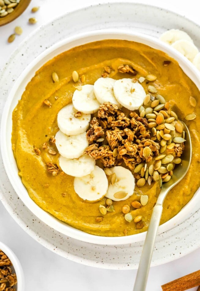 A pumpkin smoothie bowl topped with pumpkin seeds, granola and banana slices.