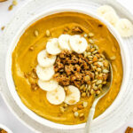 A pumpkin smoothie bowl topped with pumpkin seeds, granola and banana slices.