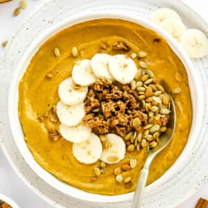 A pumpkin smoothie bowl topped with pumpkin seeds, granola and banana slices.