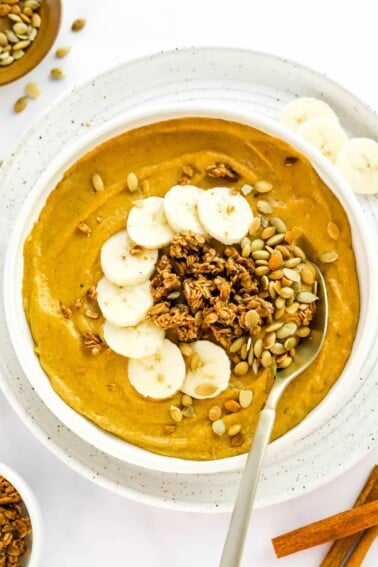 A pumpkin smoothie bowl topped with pumpkin seeds, granola and banana slices.
