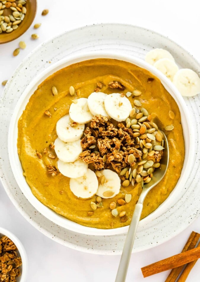 A pumpkin smoothie bowl topped with pumpkin seeds, granola and banana slices.