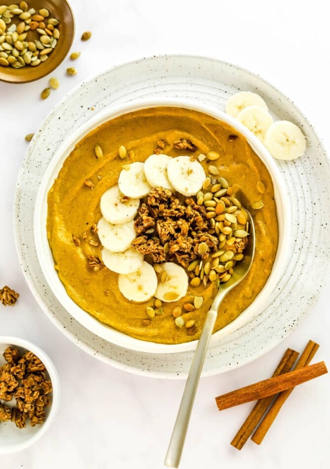 A pumpkin smoothie bowl topped with pumpkin seeds, granola and banana slices.