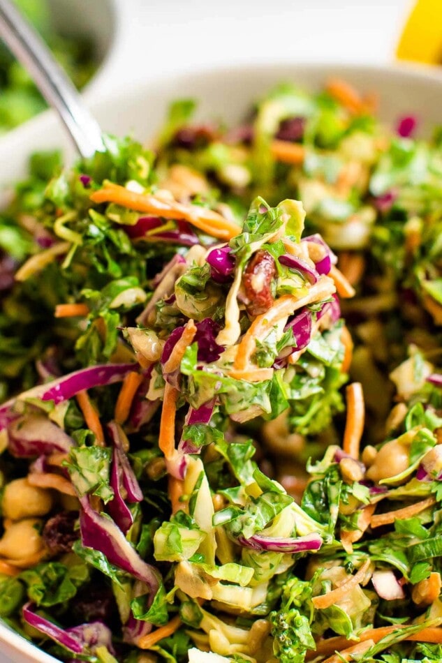 A closeup of a fork holding a bite over a bowl of sunflower crunch salad.