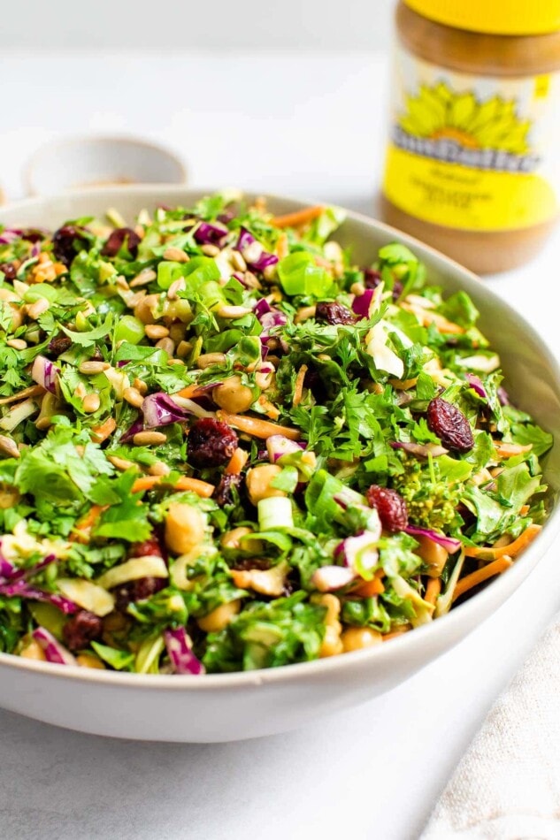 A serving bowl containing sunflower crunch salad. A container of SunButter sunflower seed butter is in the background.