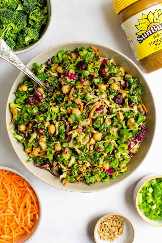 A bowl centered in the image containing sunflower crunch salad. It's surrounded by smaller bowls containing salad ingredients and a jar of SunButter..