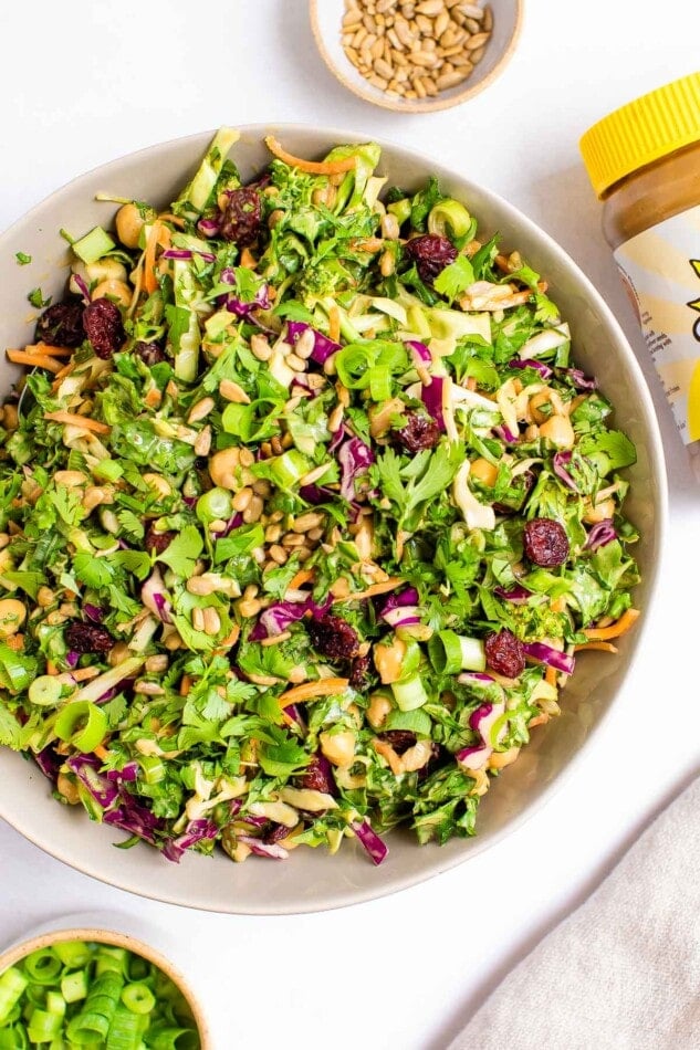 Overhead and close up view of sunflower crunch salad in a bowl. A jar of SunButter is cut out of frame.