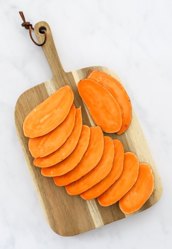 Sweet potato sliced into thin, long slices on a cutting board.