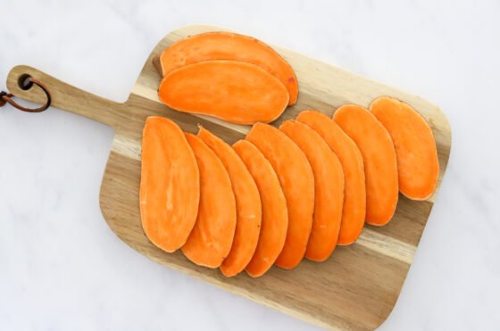 Sweet potato sliced into thin, long slices on a cutting board.