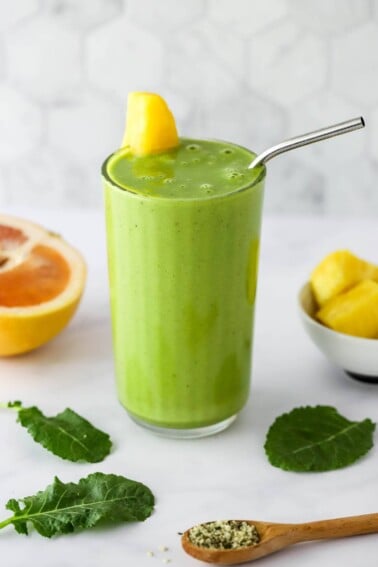 A glass containing vitamin c smoothie. It's topped with a wedge of pineapple and a straw.