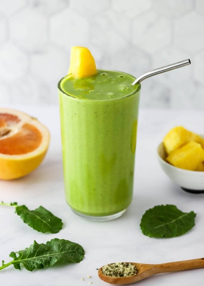 A glass containing vitamin c smoothie. It's topped witha wedge of pineapple and a straw.