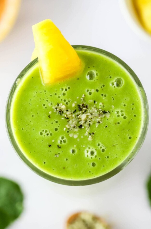 Overhead view of a vitamin c smoothie in a glass topped with a pineapple wedge and hemp seeds.