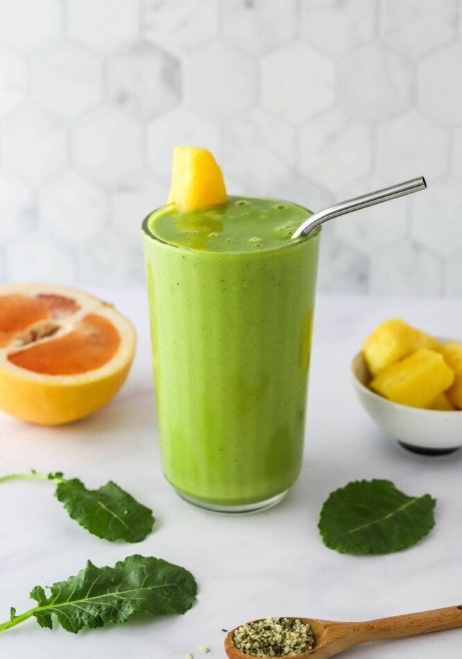 A glass of vitamin c smoothie. A pineapple wedge is on the side of the glass and a straw is sticking out of the top.