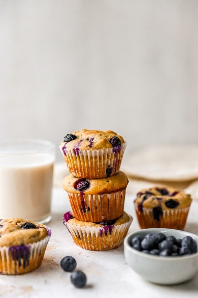 Three blueberry yogurt muffins stacked on top of each other. The muffins are lined with paper wrappers.