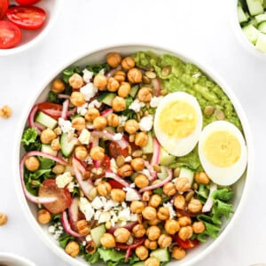 Bowl with a mashed avocado salad topped with feta, onions, egg and chickpeas.