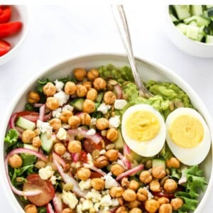 Bowl with a mashed avocado salad topped with feta, onions, egg and chickpeas.