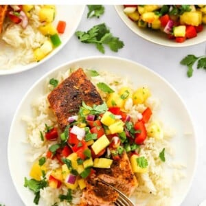 A filet of blackened salmon served over a bed of rice topped with pineapple salsa. A fork is removing a bite.