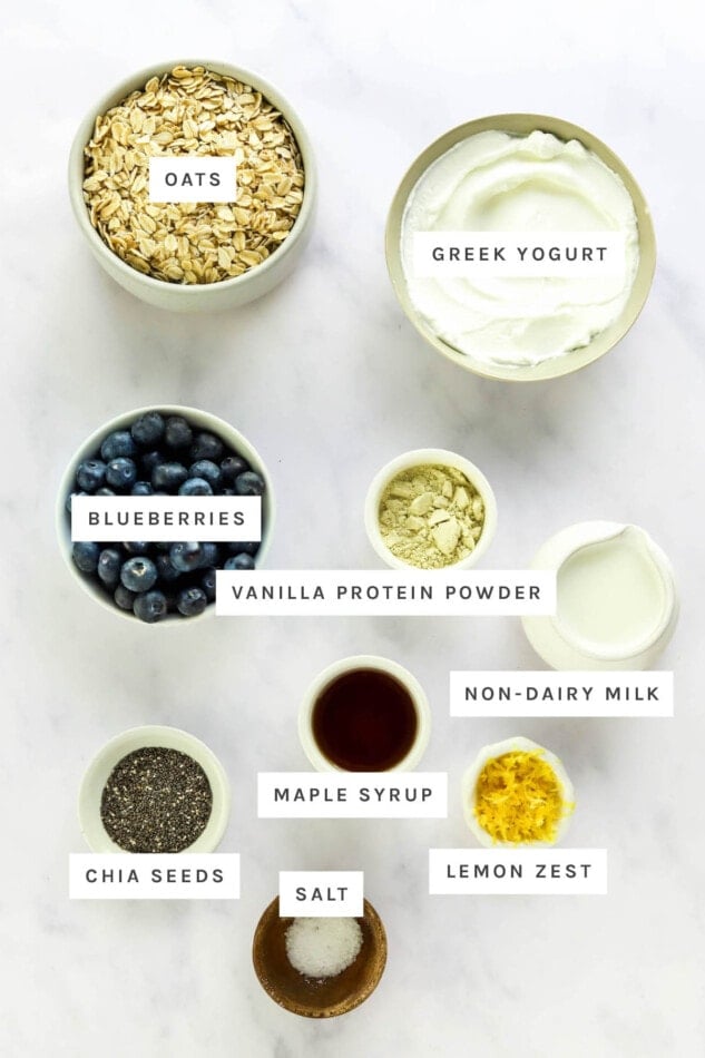 Ingredients measured out to make Blueberry Lemon Overnight Oats: oats, Greek yogurt, blueberries, vanilla protein powder, non-dairy milk, maple syrup, lemon zest, chia seeds and salt.