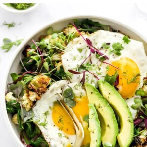 Salad topped with sunny-side-up eggs and avocado.