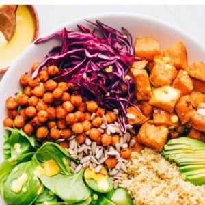 A buddha bowl with sweet potatoes, spinach, sunflower seeds, shredded red cabbage, chickpeas, cucumbers, quinoa and avocado. A fork rests in the bowl.