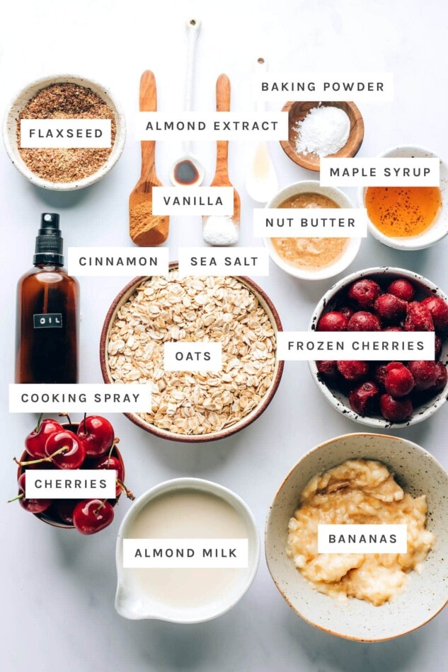 Ingredients measured to make cherry baked oatmeal: flaxseed, almond extract, baking powder, vanilla, maple syrup, nut butter, cinnamon, sea salt, oats, cooking spray, frozen cherries, cherries, almond milk and bananas.