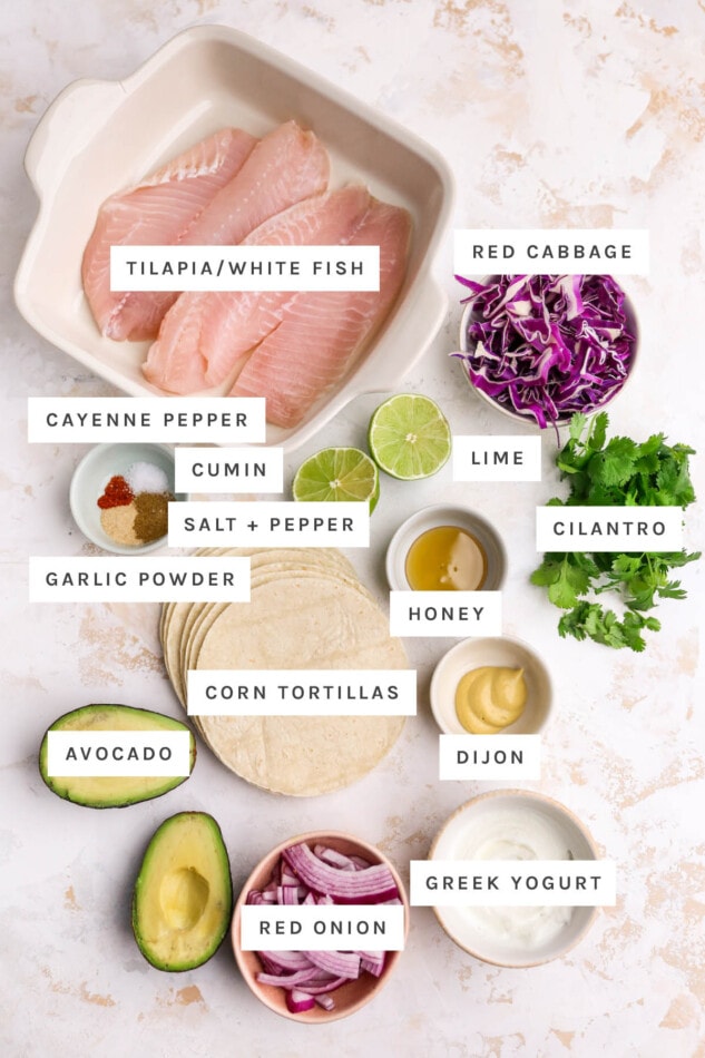 Ingredients measured out to make Healthy Fish Tacos: tilapia, cabbage, cayenne pepper, cumin, salt, pepper, garlic powder, lime, cilantro, honey, corn tortillas, dijon, avocado, red onion and Greek yogurt.