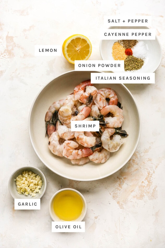 Ingredients measured out to make grilled shrimp: salt, pepper, cayenne pepper, lemon, onion powder, Italian seasoning, shrimp, garlic and olive oil.