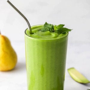 A glass containing pear smoothie, a metal straw sticks out of the glass.