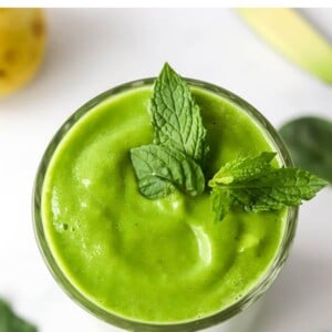 An overhead view of a drinking glass containing pear smoothie topped with fresh mint leaves.