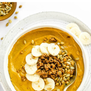 A pumpkin smoothie bowl topped with pumpkin seeds, granola and banana slices.