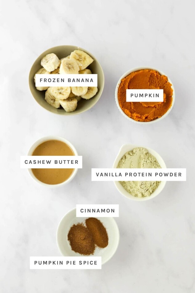 Ingredients measured out to make a pumpkin smoothie bowl: frozen banana, pumpkin, cashew butter, vanilla protein powder, cinnamon and pumpkin pie spice.