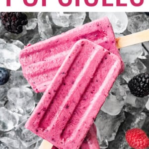 Three berry Greek yogurt popsicles on top of ice. Some berries are scattered around.
