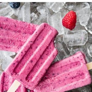 Several berry Greek yogurt popsicles on top of ice. One popsicle has a bite taken out of it.