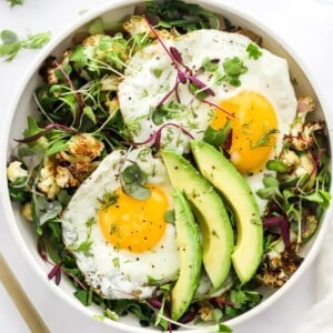 A breakfast salad bowl topped with eggs and avocado.