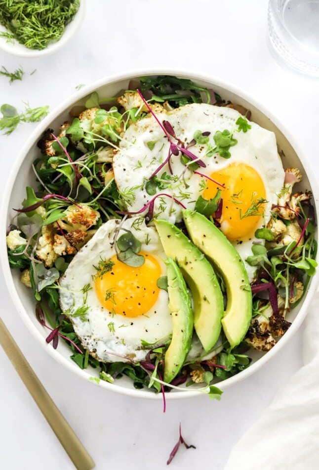 A breakfast salad bowl topped with eggs and avocado.