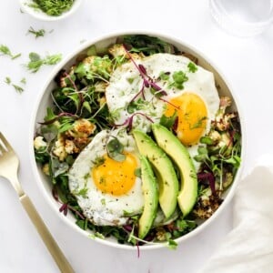 A breakfast salad bowl topped with eggs and avocado.