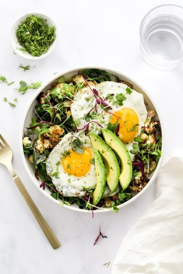 A breakfast salad bowl topped with eggs and avocado.