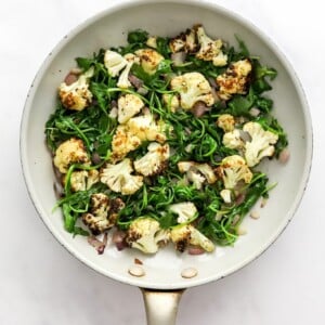 Sautéing spinach and cauliflower in a pan with onion and garlic.
