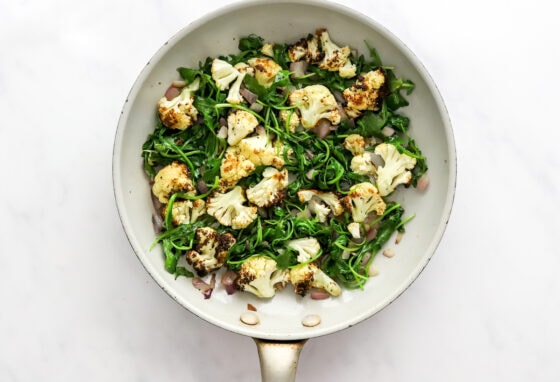 Sautéing spinach and cauliflower in a pan with onion and garlic.