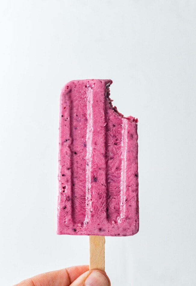 A popsicle held up by a hand with a bite taken out of it.