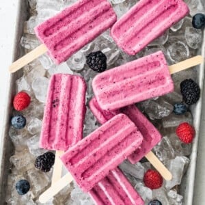Overhead view of popsicles and berries scattered overtop of ice.