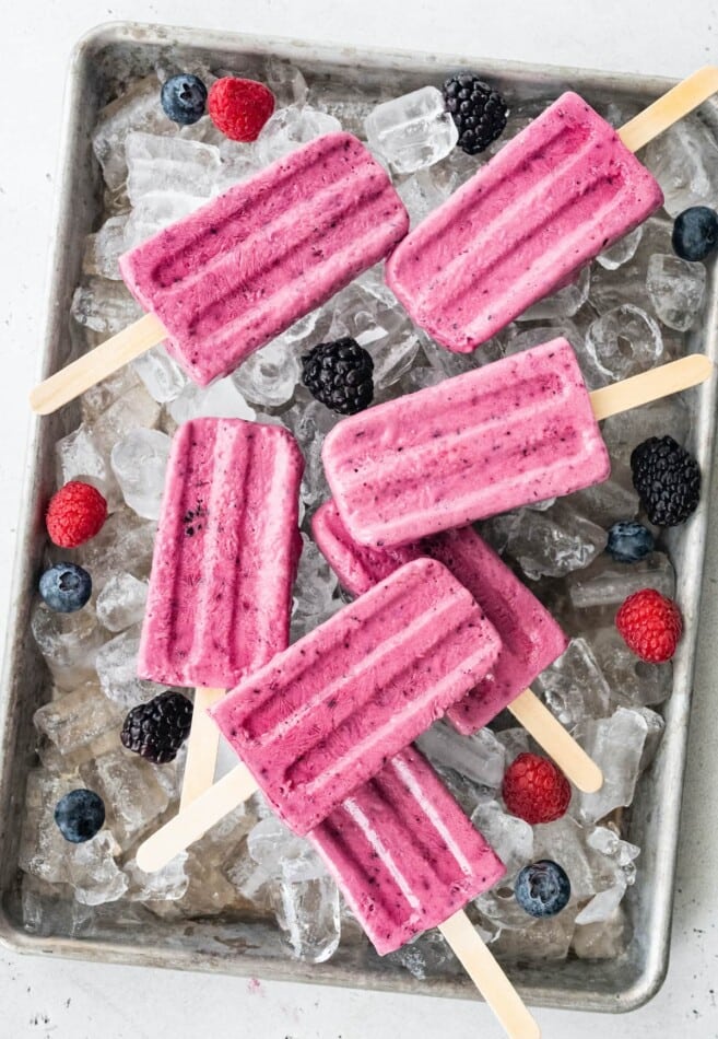 Overhead view of popsicles and berries scattered overtop of ice.
