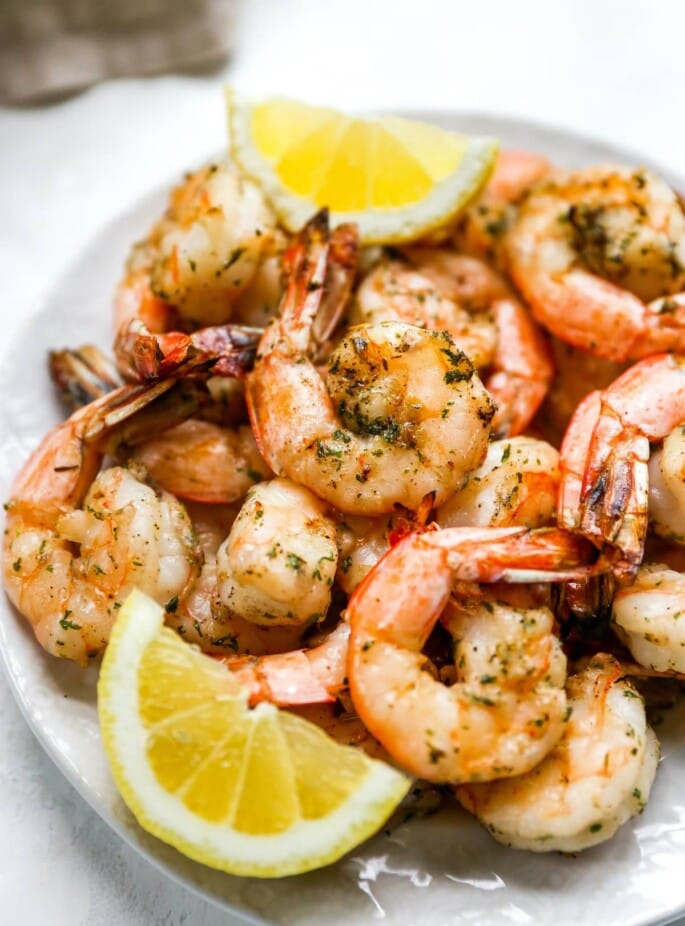 Close up of grilled shrimp on a plate with lemon wedges.