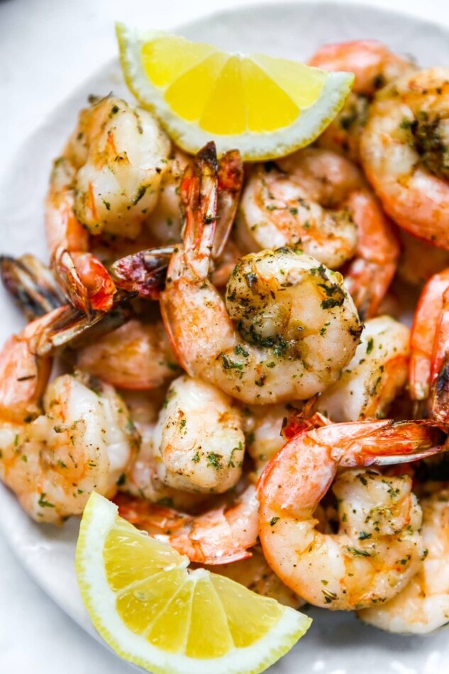 Closeup of grilled shrimp on a plate with lemon wedges.