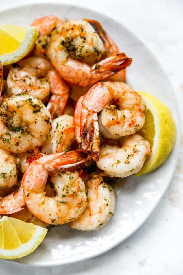 Grilled shrimp on a plate with lemon wedges.