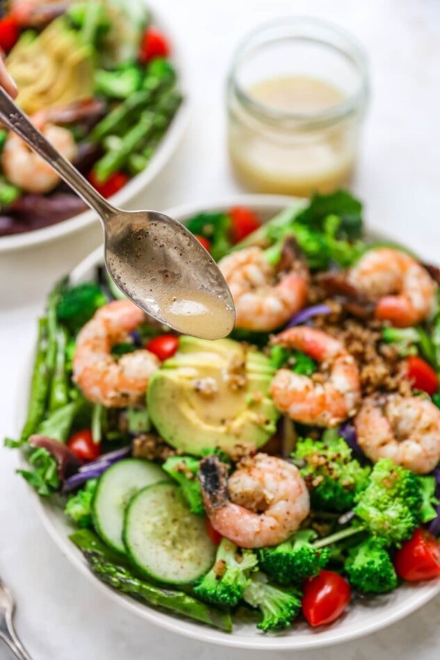 Drizzling dressing onto a bowl of grilled shrimp salad.