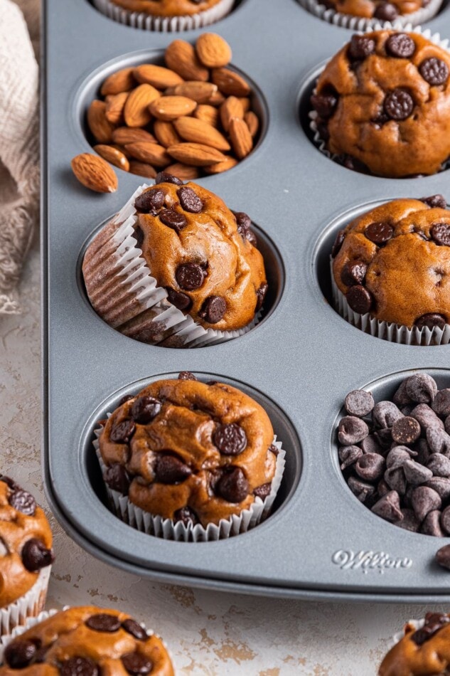 Protein muffins in a muffin tin, some of the cavities contain chocolate chips and almonds instead of a muffin.