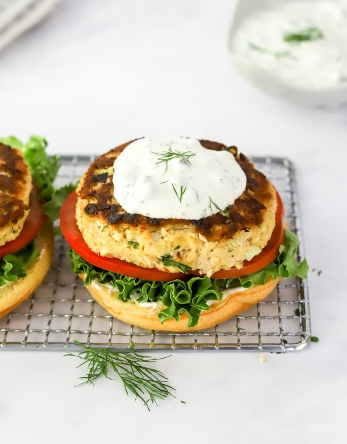A salmon burger assembled on a wire rack, it's topped with an herb sauce.